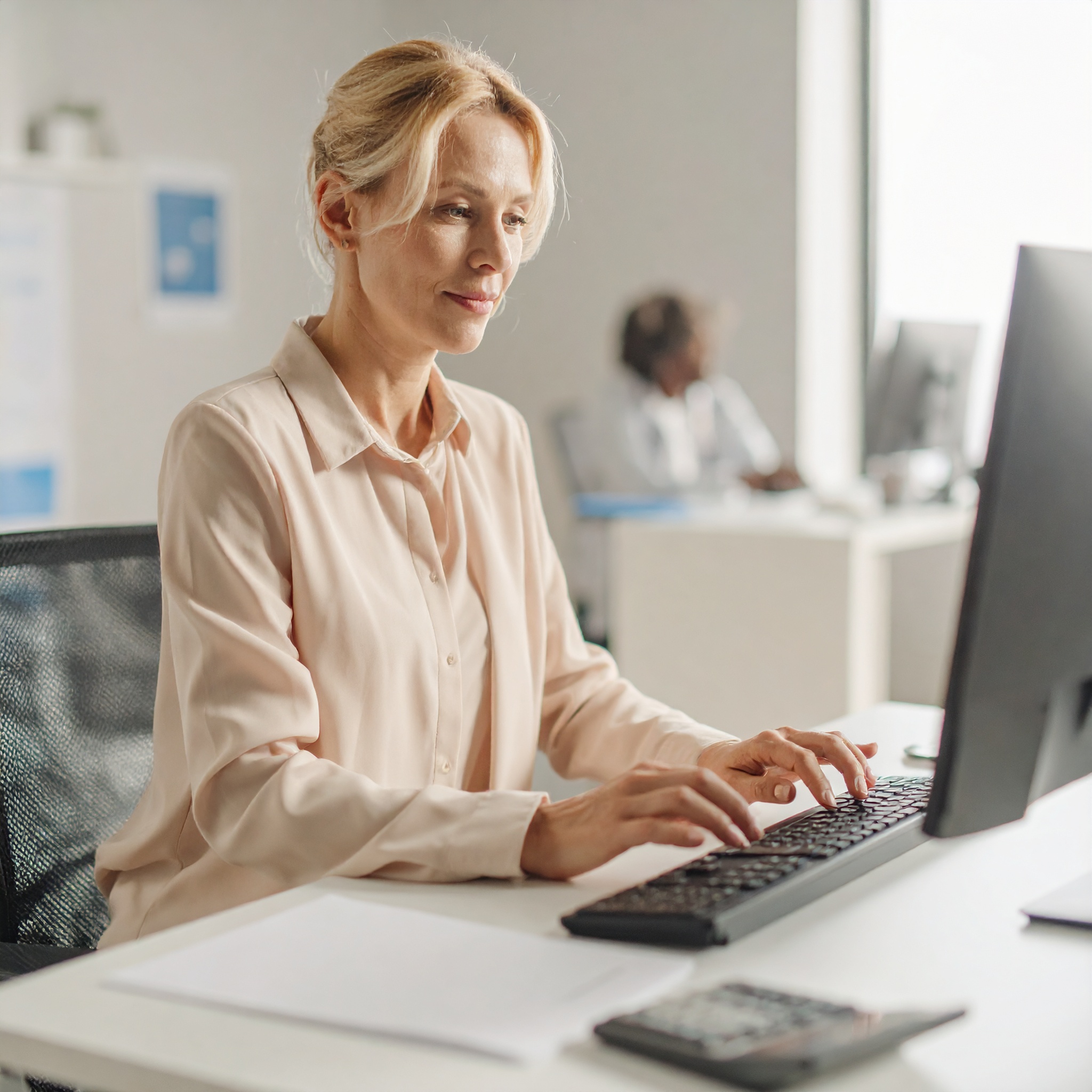 Eine Frau im Büro tippt an ihrem Schreibtisch auf einer Tastatur