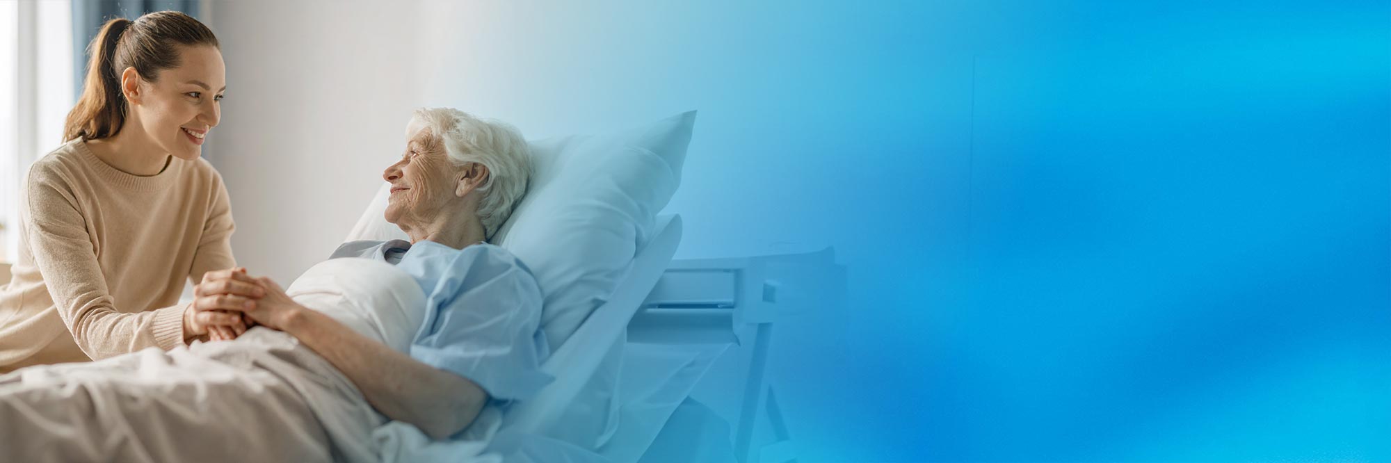 Eine junge Frau unterhält sich mit einer älteren Dame im Krankenhauszimmer. Das BIld hat einen Verlauf in eine blaue Farbe.