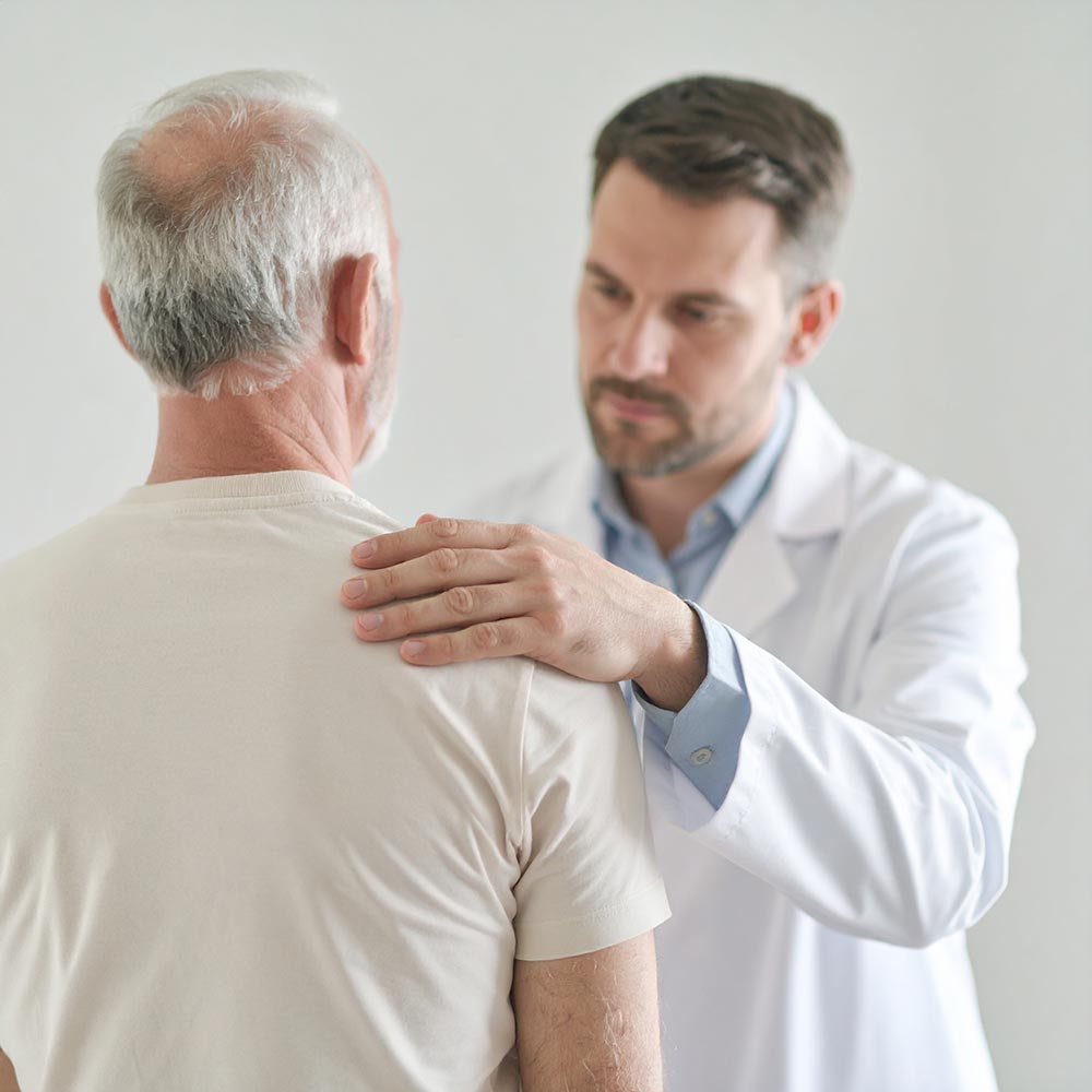 Ein Physiotherapeut unterstützt einen Patienten bei Bewegungsübungen an der Schulter.