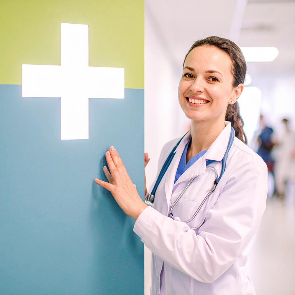 Freundliche Ärztin im Klinikflur steht neben einem medizinischen Hinweisschild